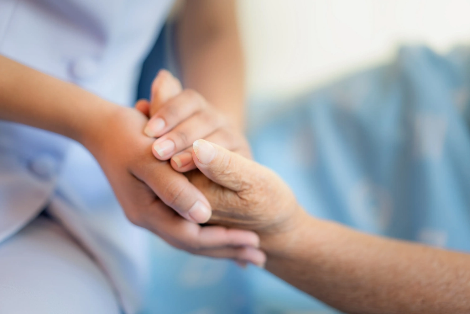 Curanus GmbH - Pflege - Krankenschwester sitzt auf einem Krankenhausbett neben einer älteren Frau und hilft ihr, Pflegekonzept für ältere Menschen
